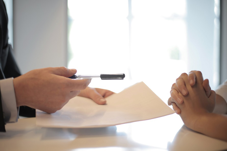 Two pairs of hands holding a contract and pen